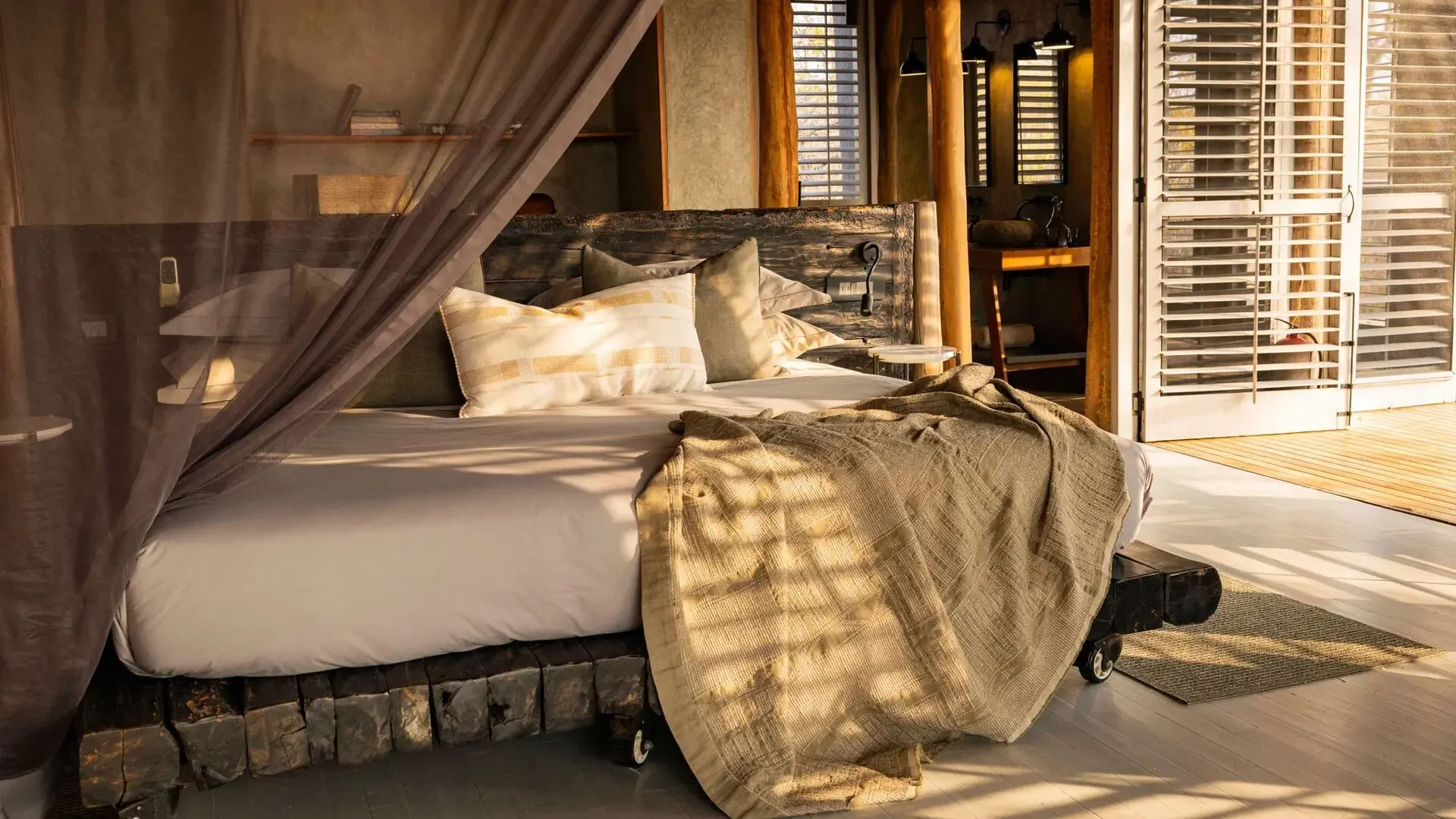 A bed draped with mosquito netting beside timber shutters