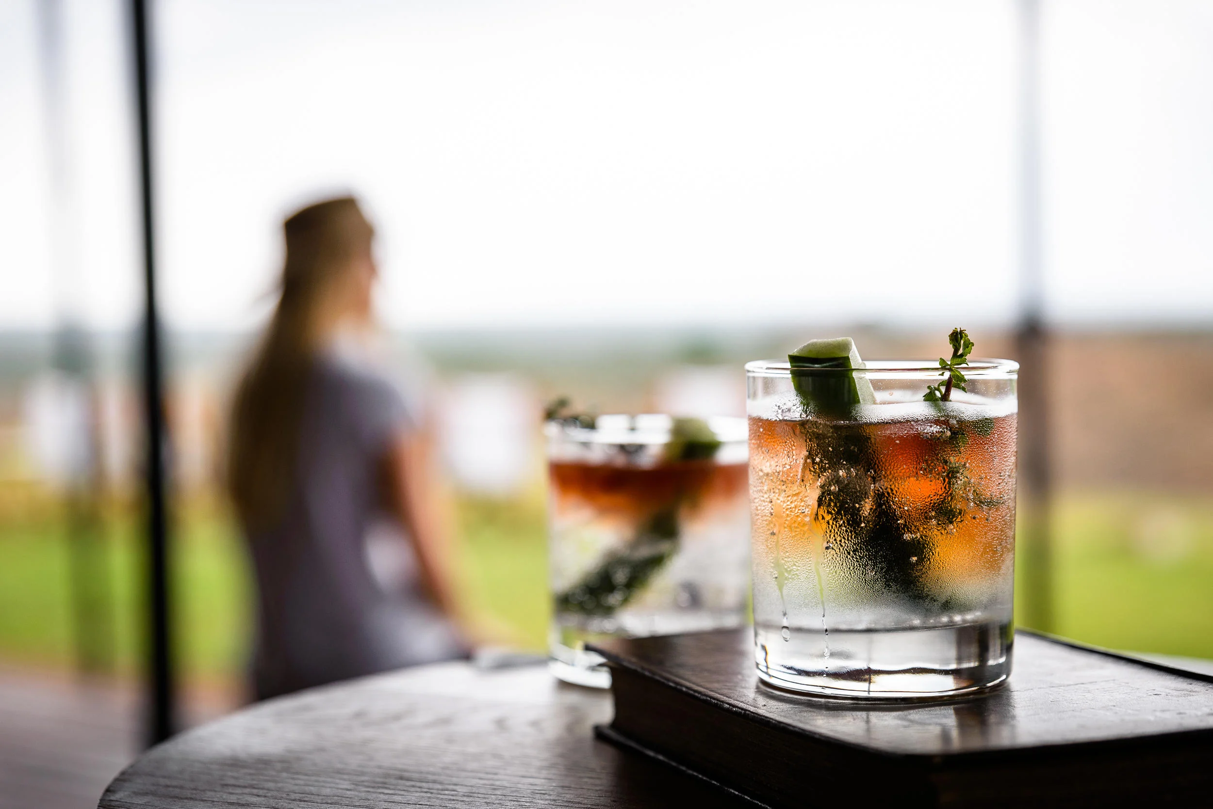 Two drinks on a table with a guest looking out beyond