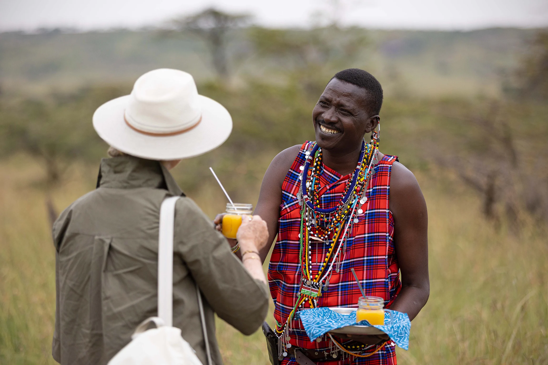 A Maasai host welcoming a guest with a drink