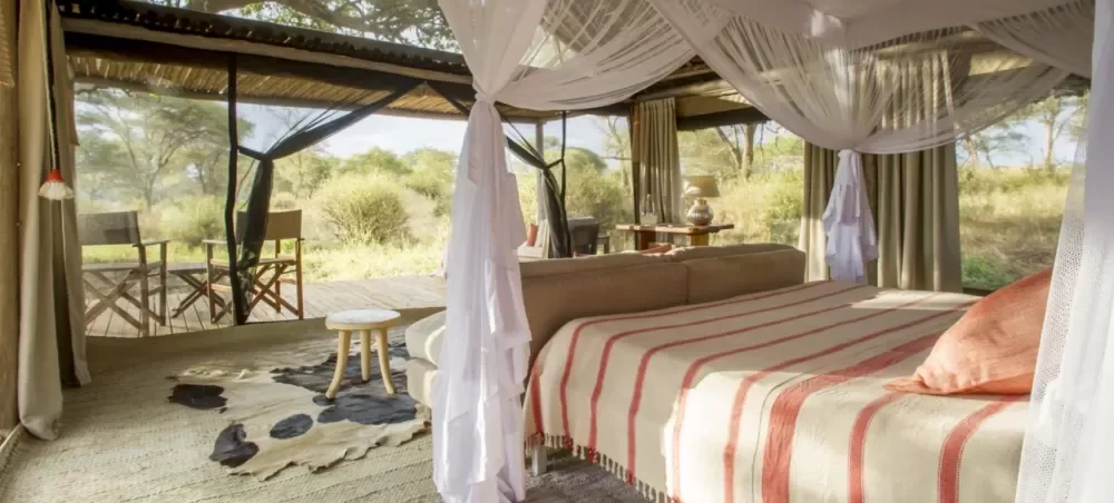 A tent bedroom with a canopied bed and chairs on the deck