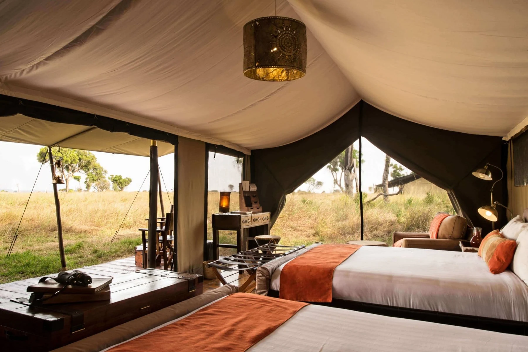 A tent bedroom with an orange throw, open to the view