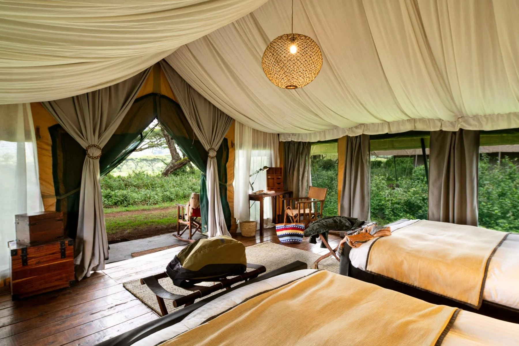 A tent bedroom with drapes and the forest beyond