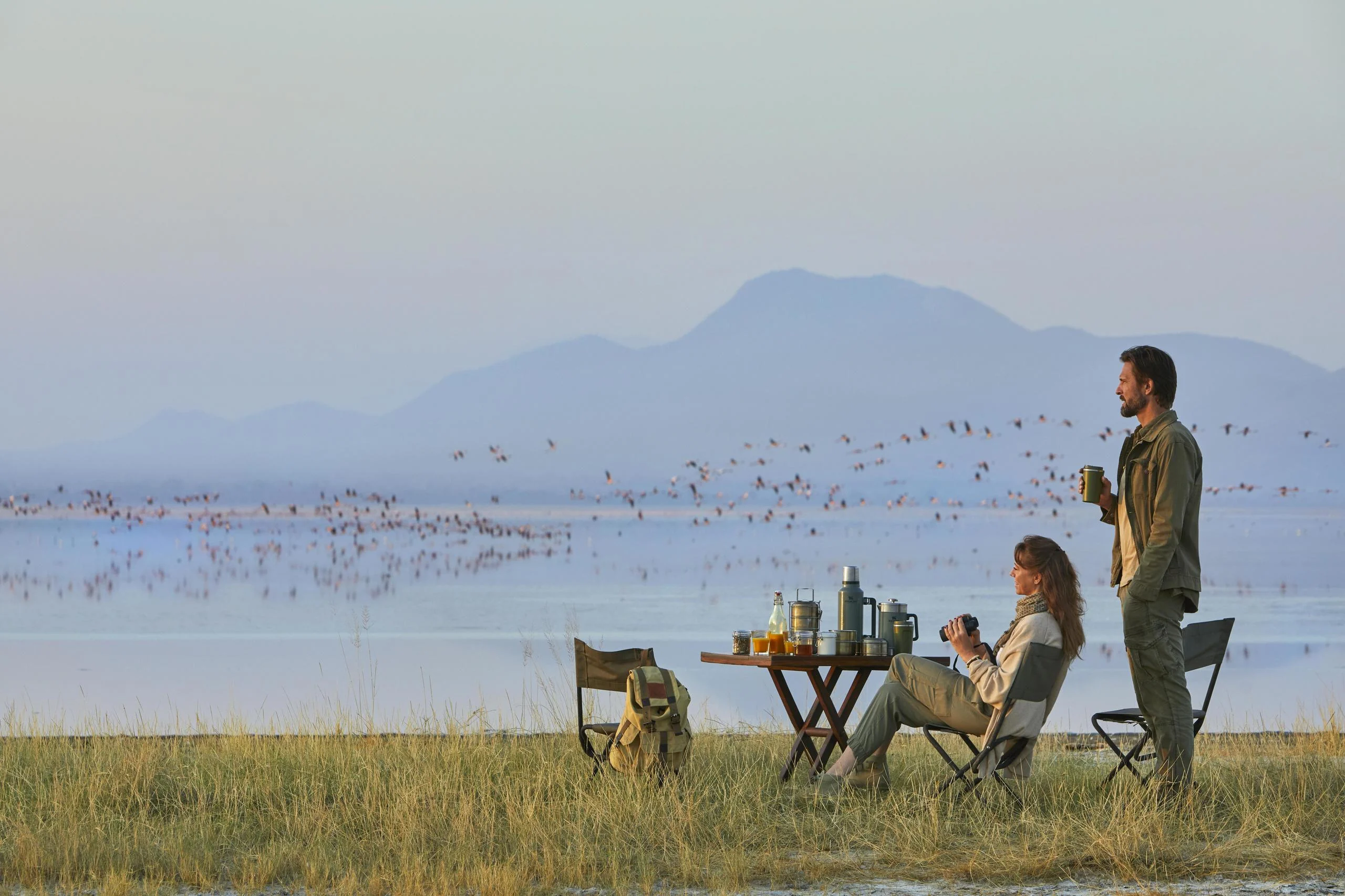 Two guests at a table on the lakeshore with flamingo beyond