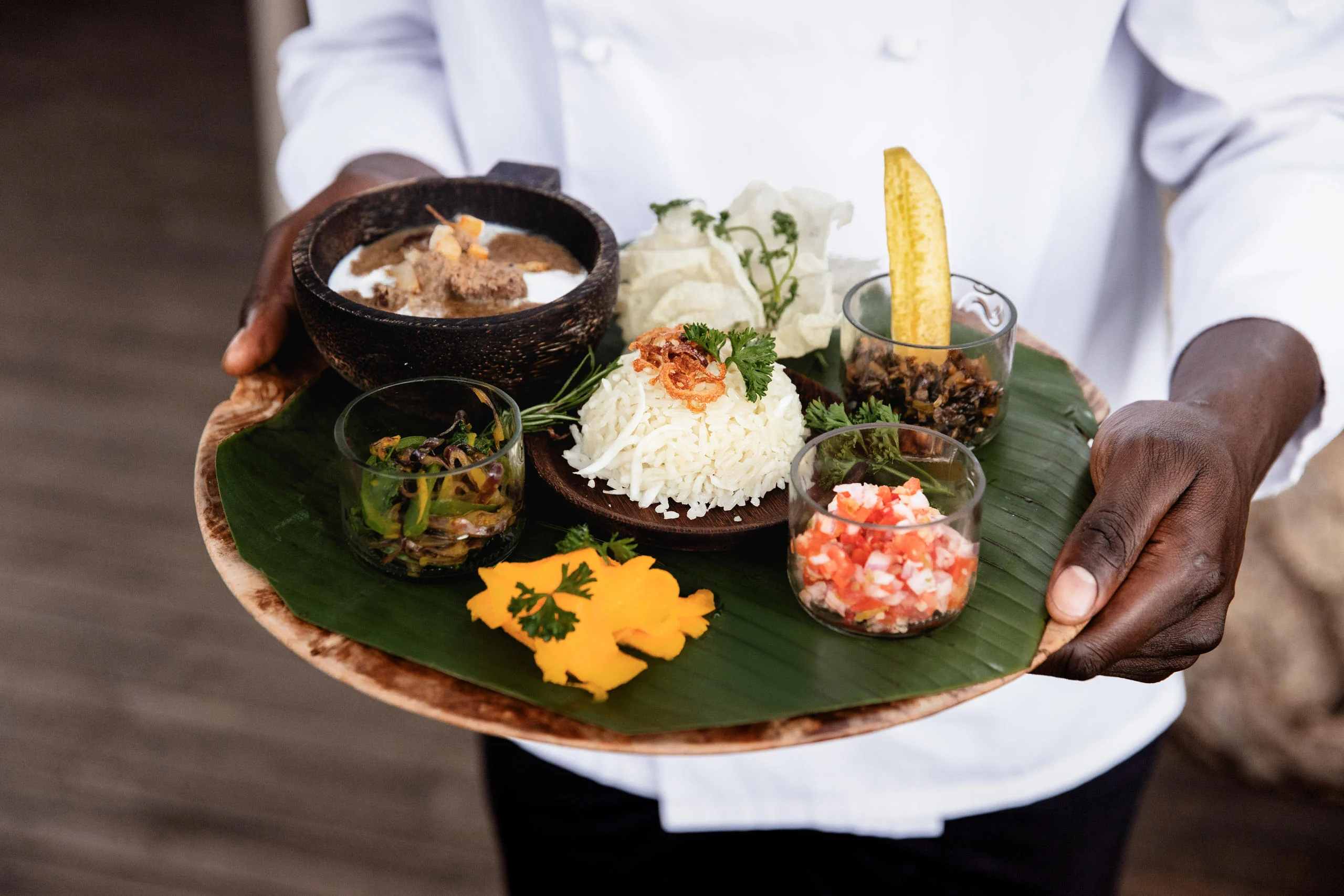 A member of staff holding a plate of food on a banana leaf