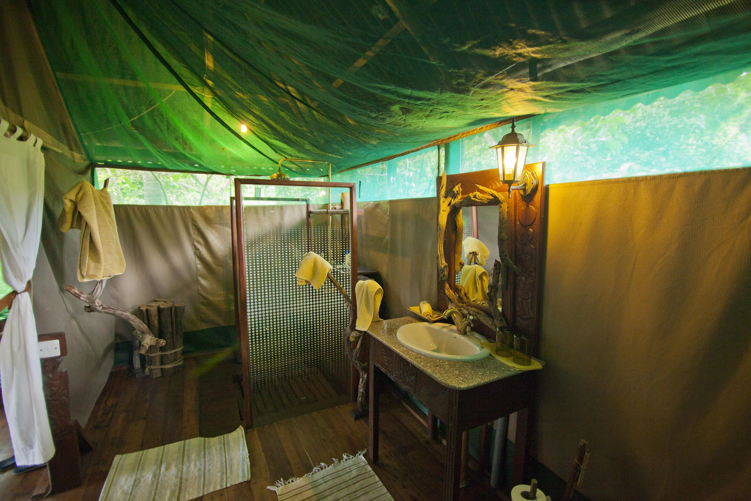 A tent bathroom with a basin beneath a green canvas roof