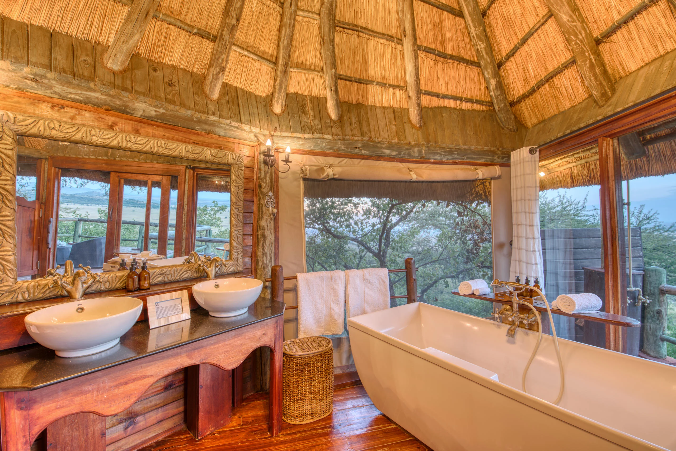 A bathroom with twin basins and a bath under thatch