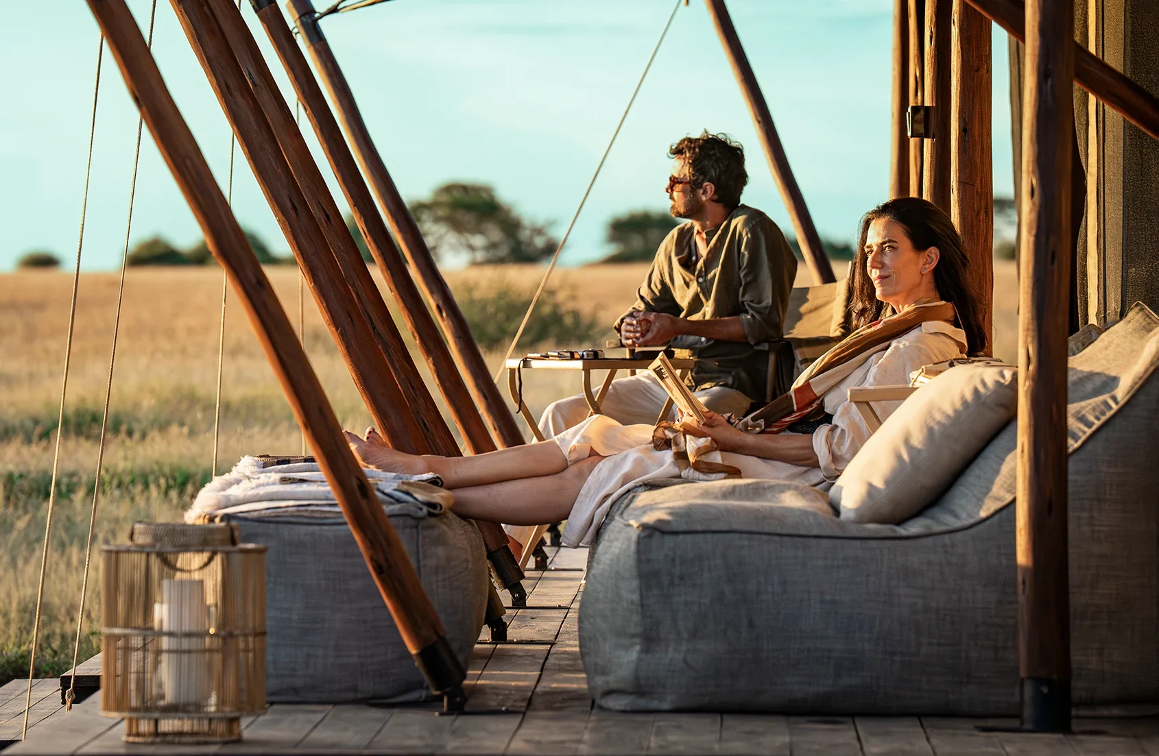 Two guests on the sofa of a tent deck, looking over the plains