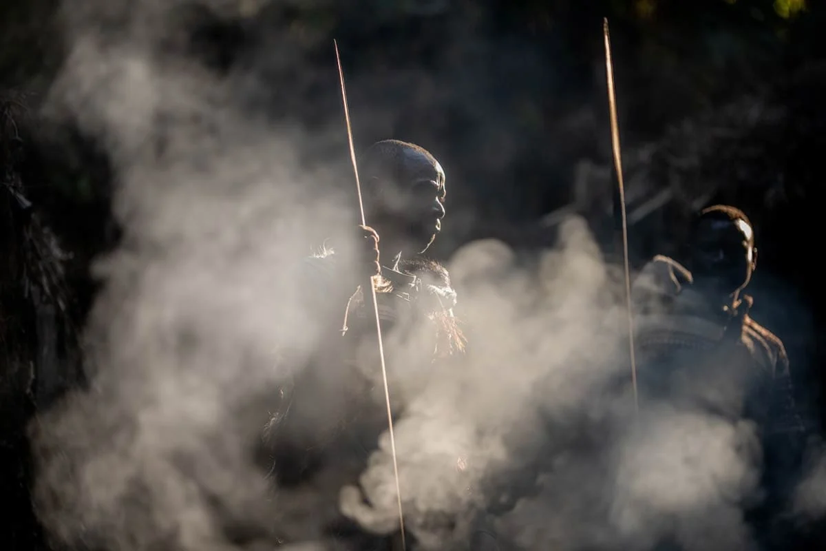 Batwa men with spears in the smoke of a fire