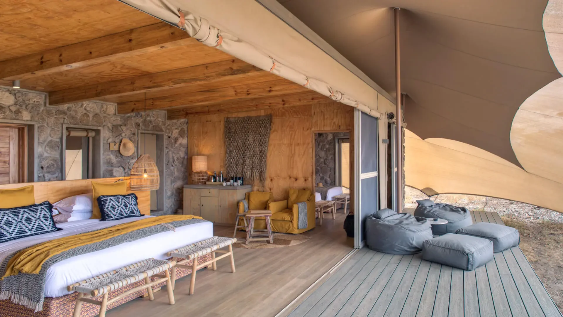 A tent with the bed, sofa and deck looking over the grassland
