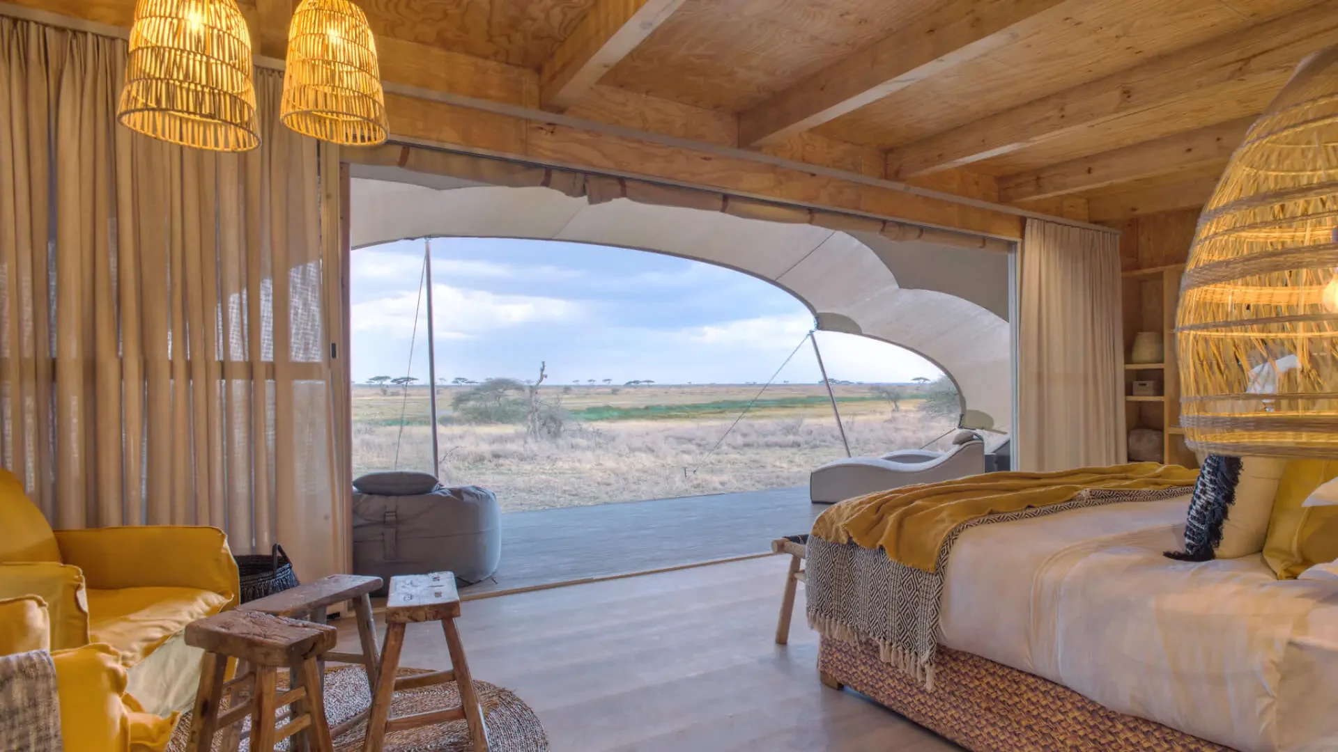A tent bedroom with woven lampshades and the view beyond