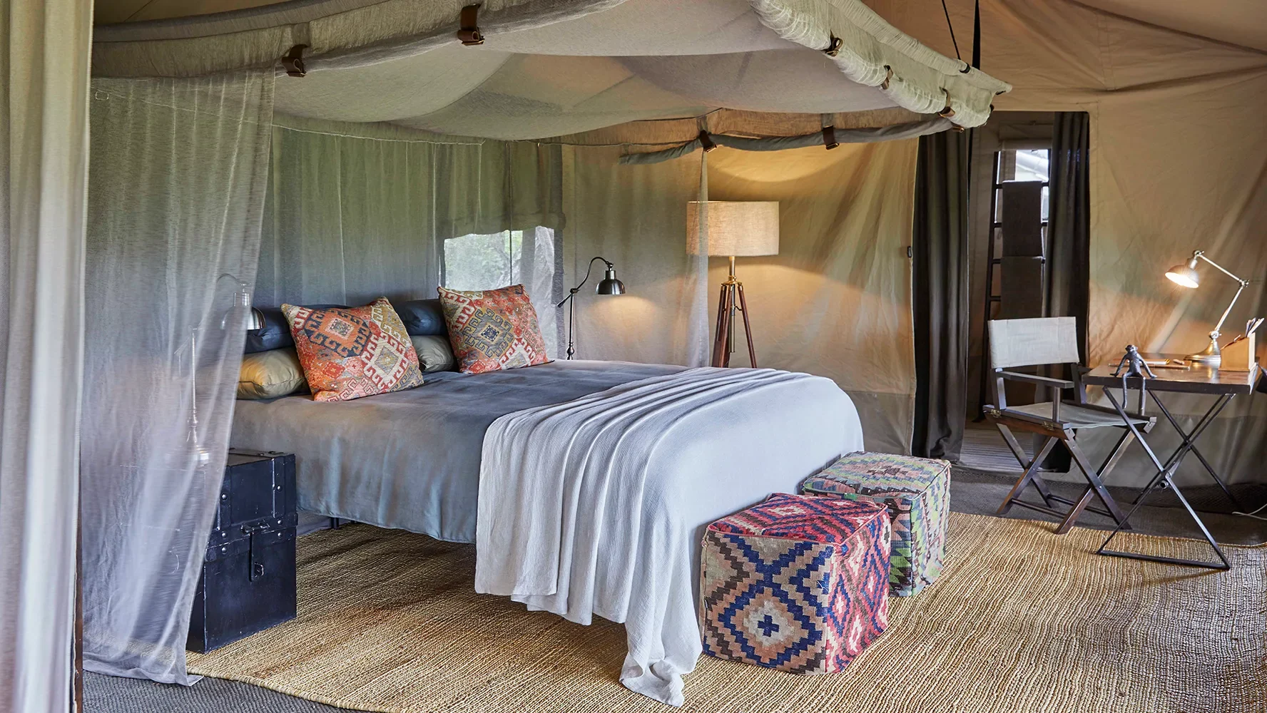 A tent bedroom with patterned cushions and a lamp