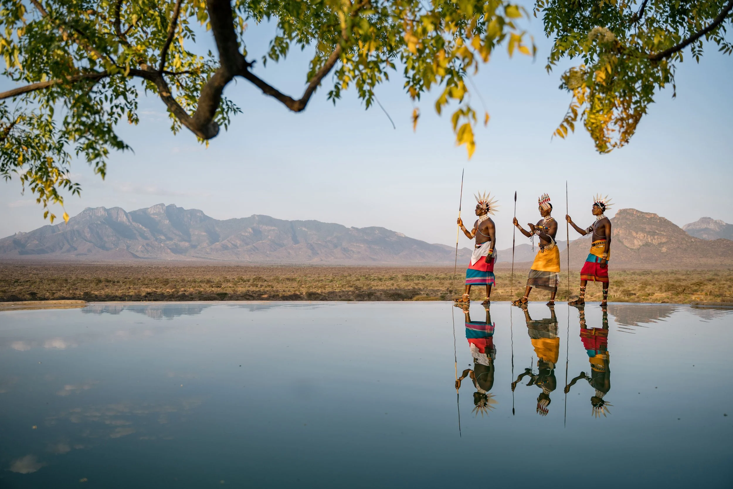 Samburu warriors reflected in the pool with the hills beyond