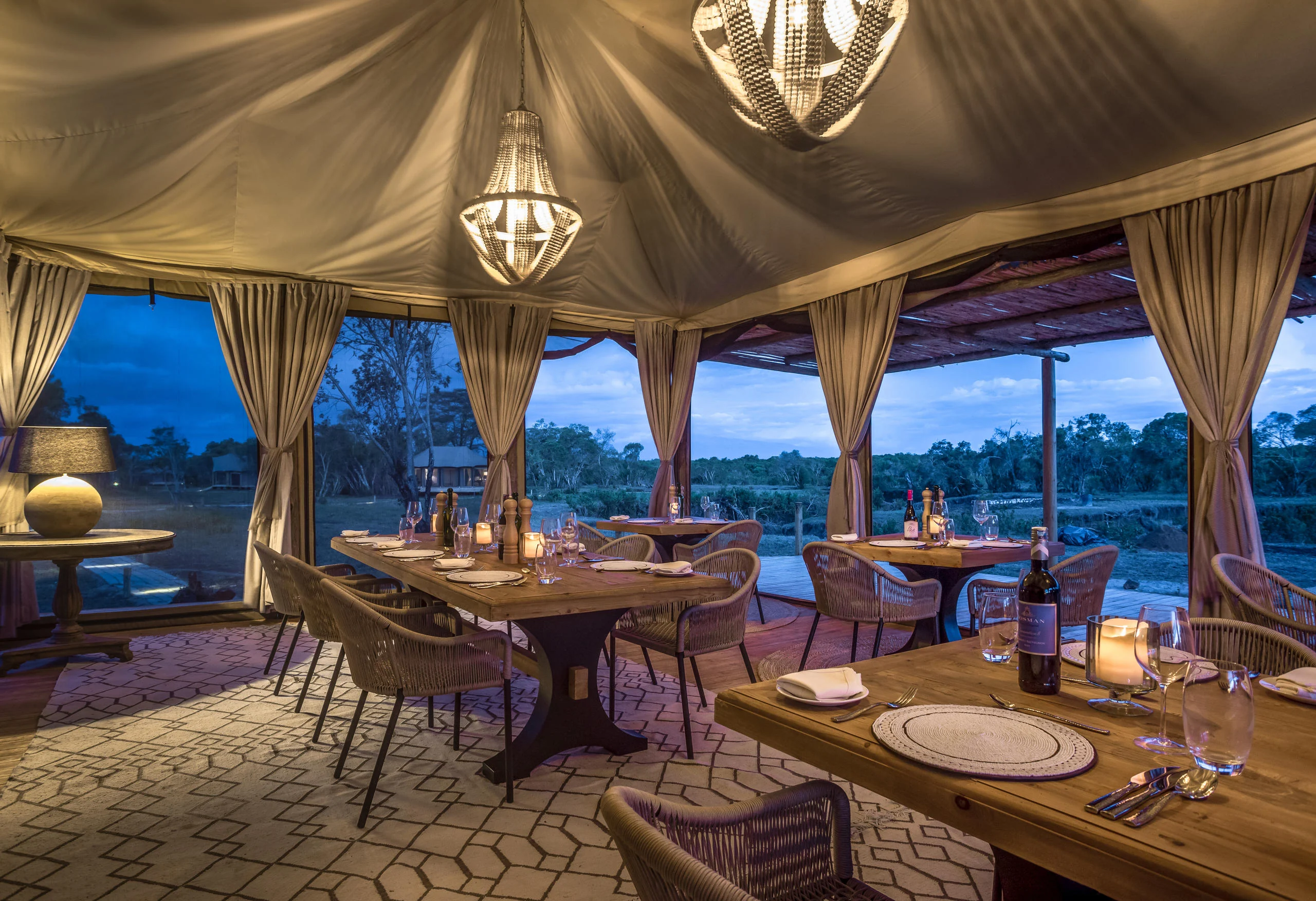 The dining tent lit at dusk with the river beyond