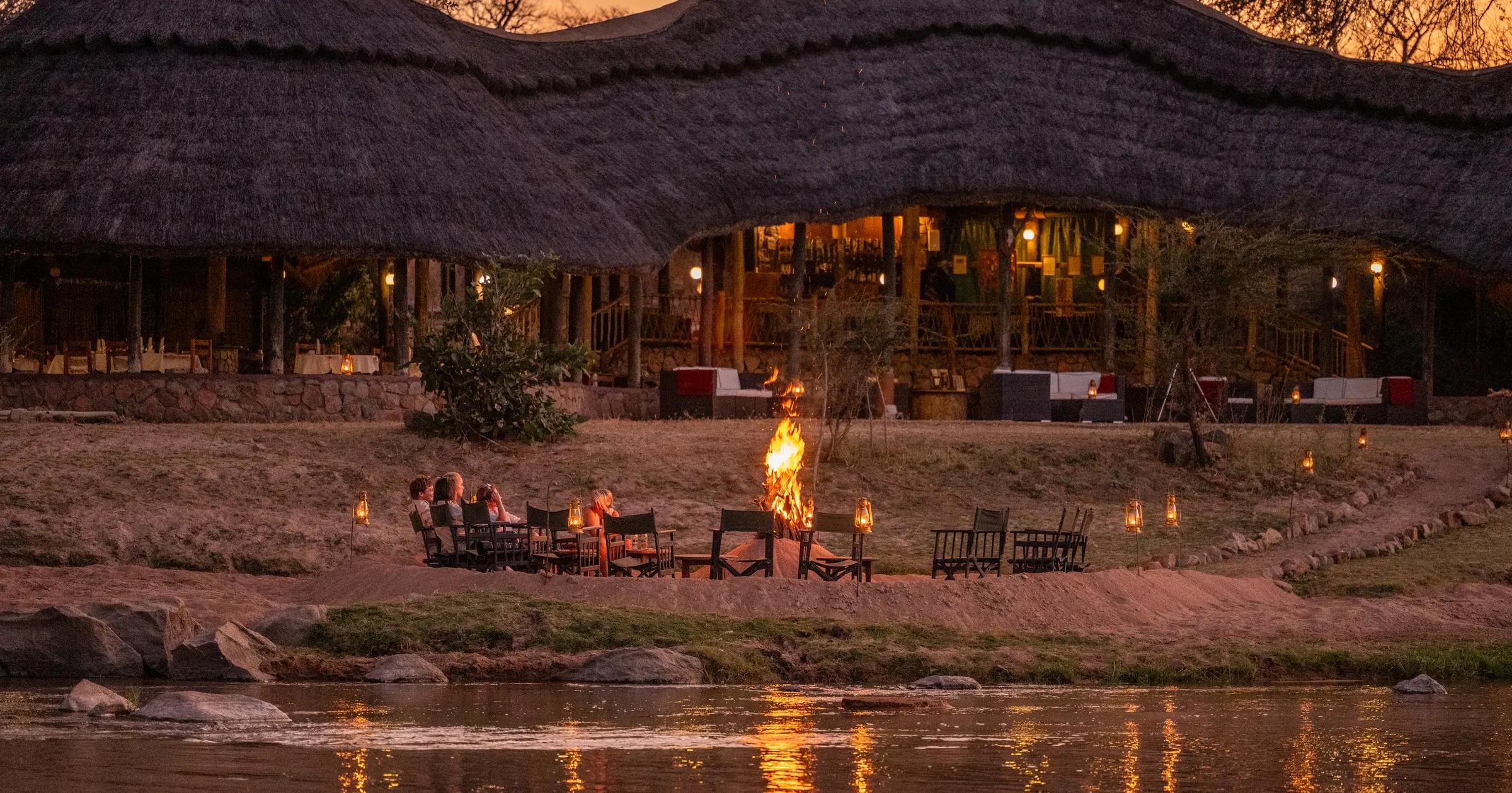 The thatched main building lit at dusk beside the river