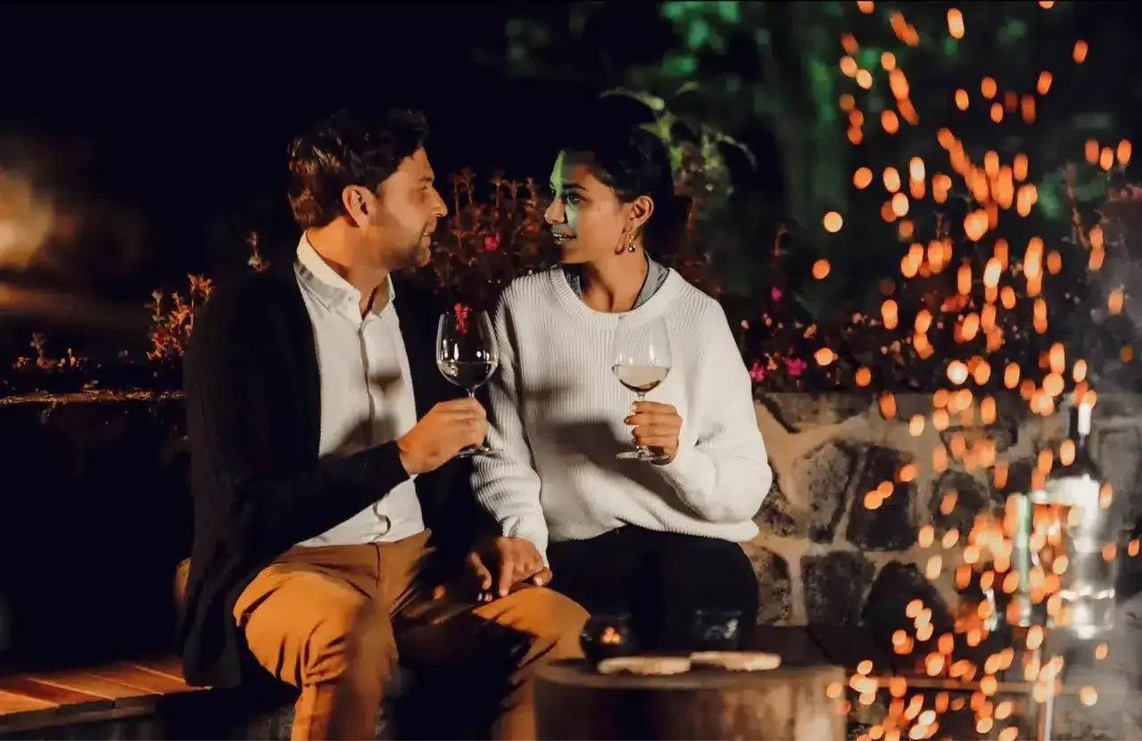 Two guests with drinks beside the fire in the evening