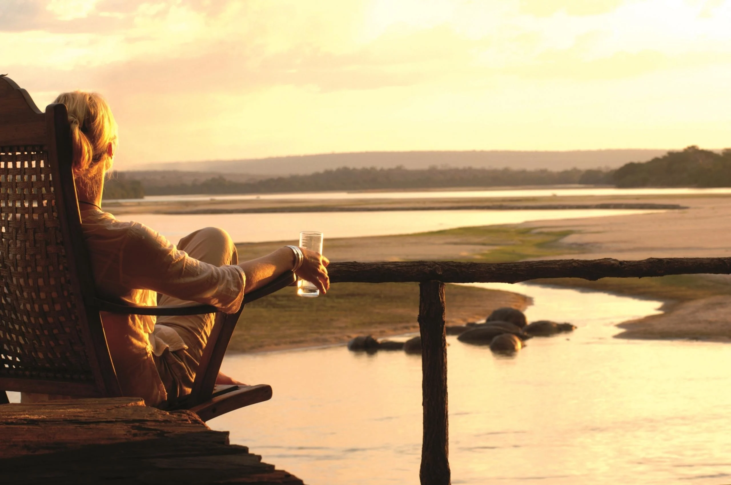 A guest with a drink on a deck above the river at sunset