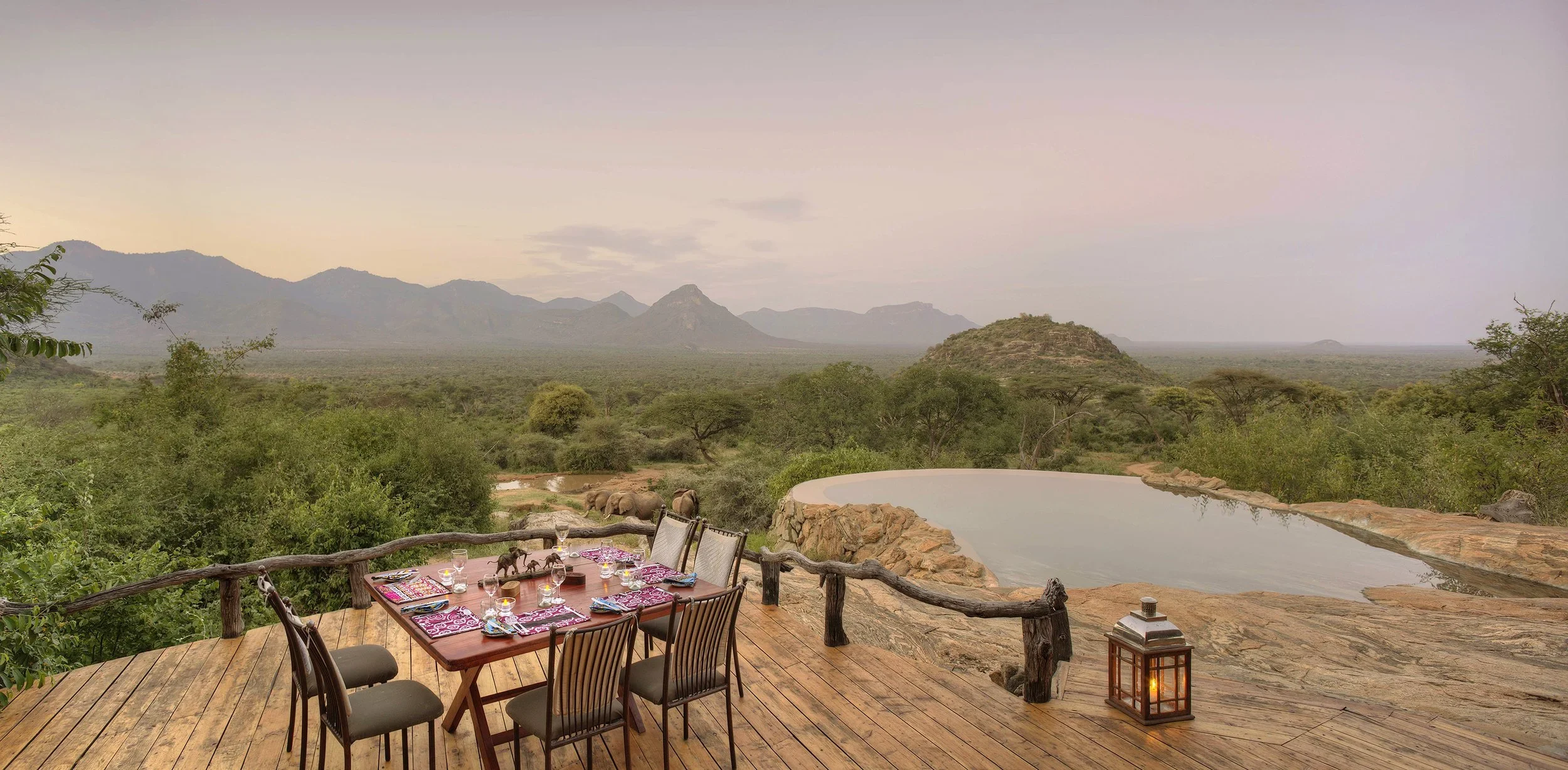 A table laid on the deck above the pool, with the hills beyond