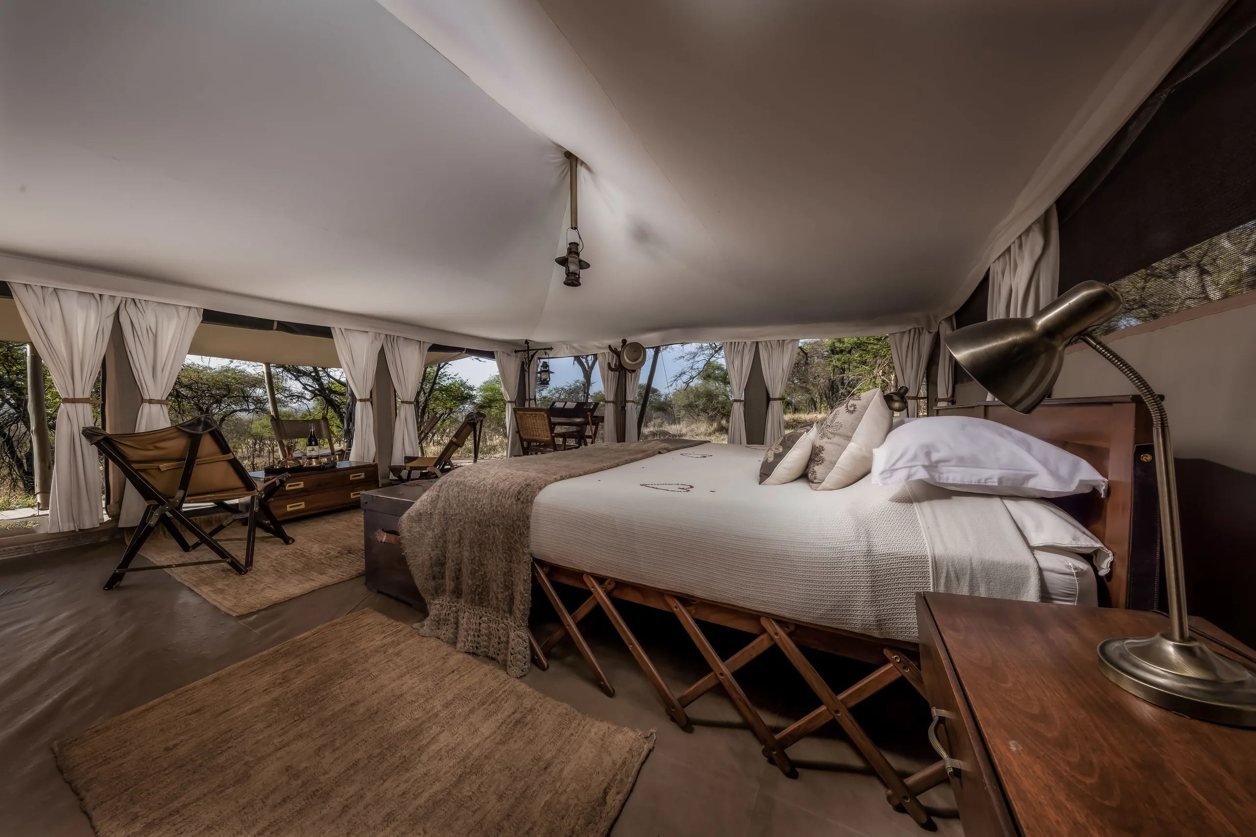 A double bed and sitting area inside a guest tent at Serengeti Pioneer Camp
