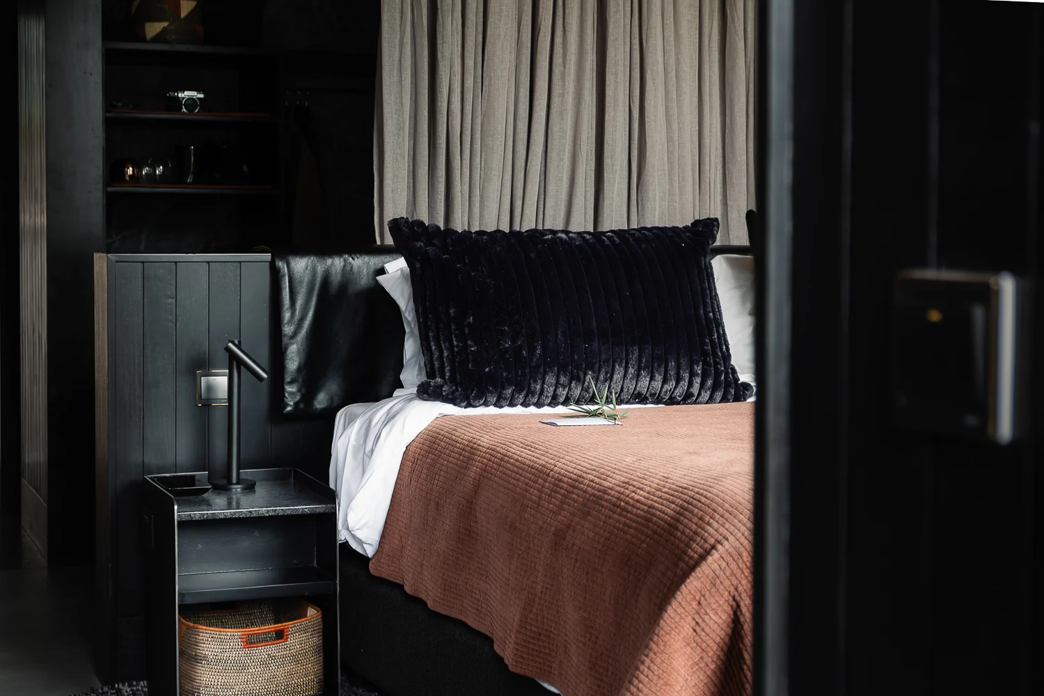 A bedroom with a rust-coloured bedspread and dark timber walls