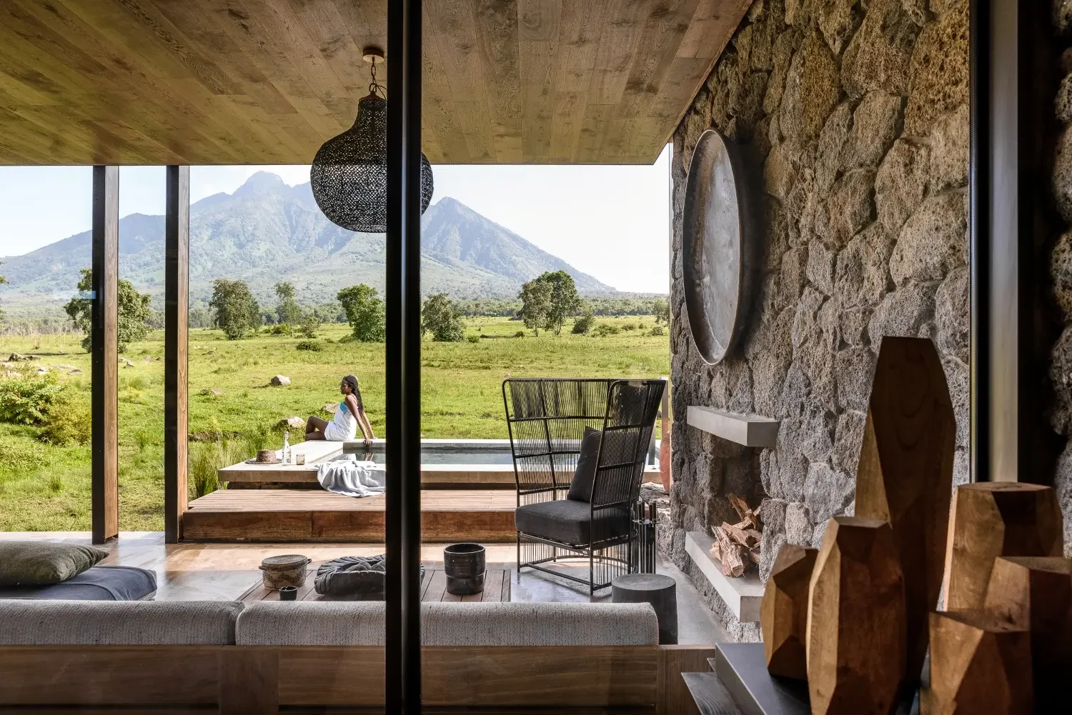 A suite with glass walls and a stone fireplace, with a volcano beyond