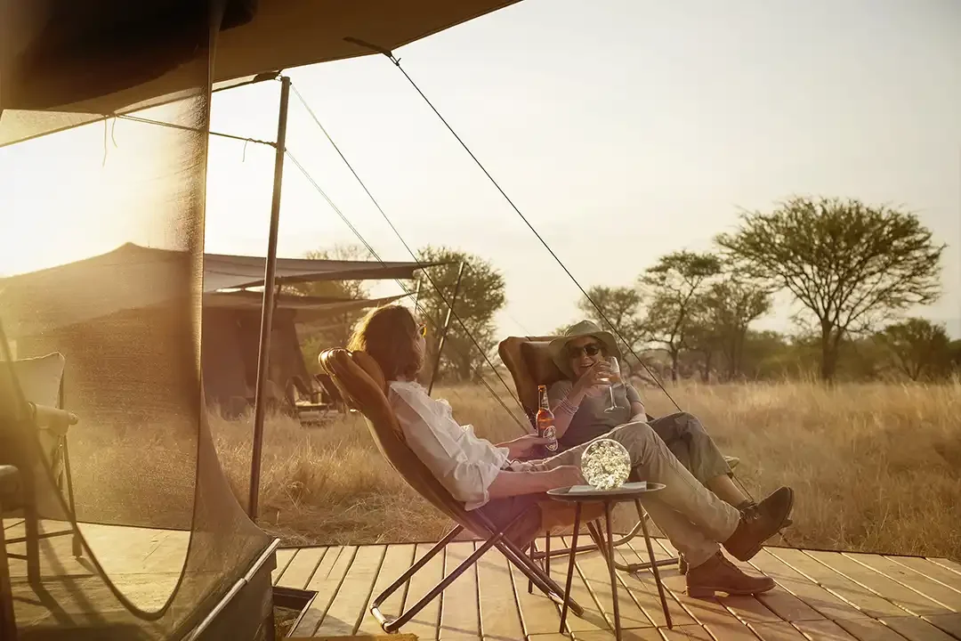 Two guests on the deck of a tent, looking over the plains