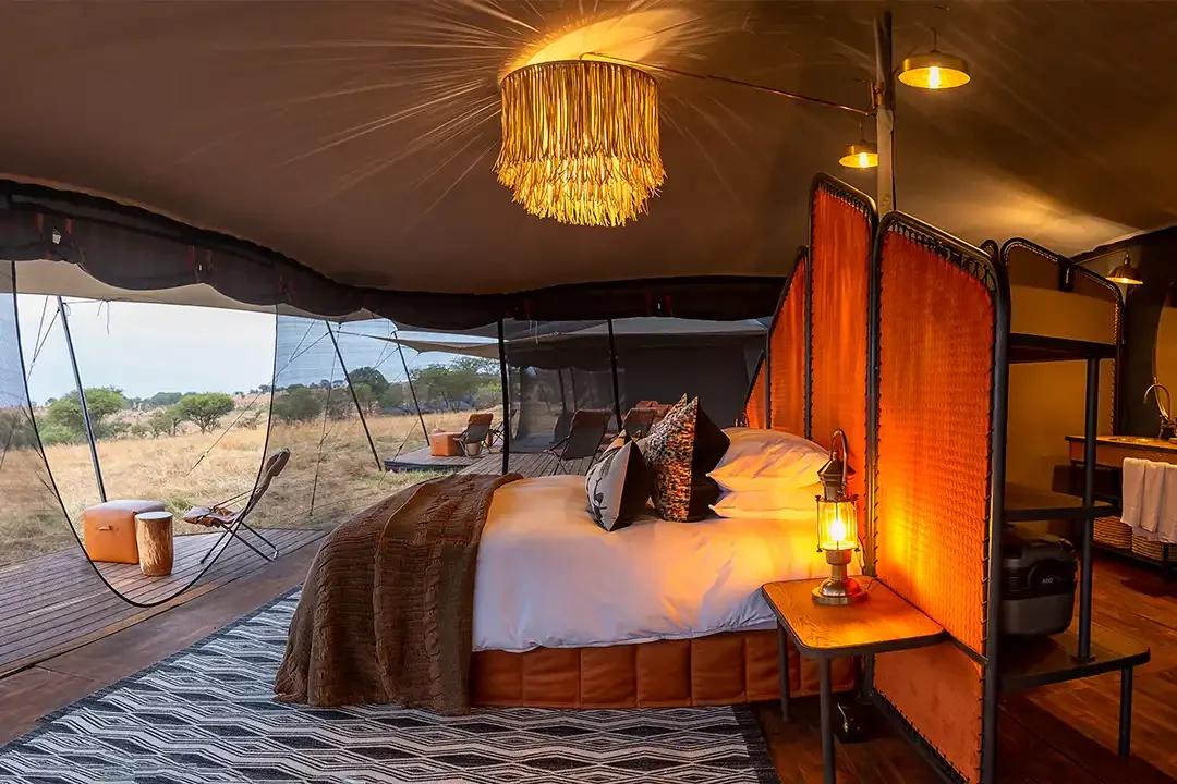 A tent bedroom with a lantern and the plains beyond