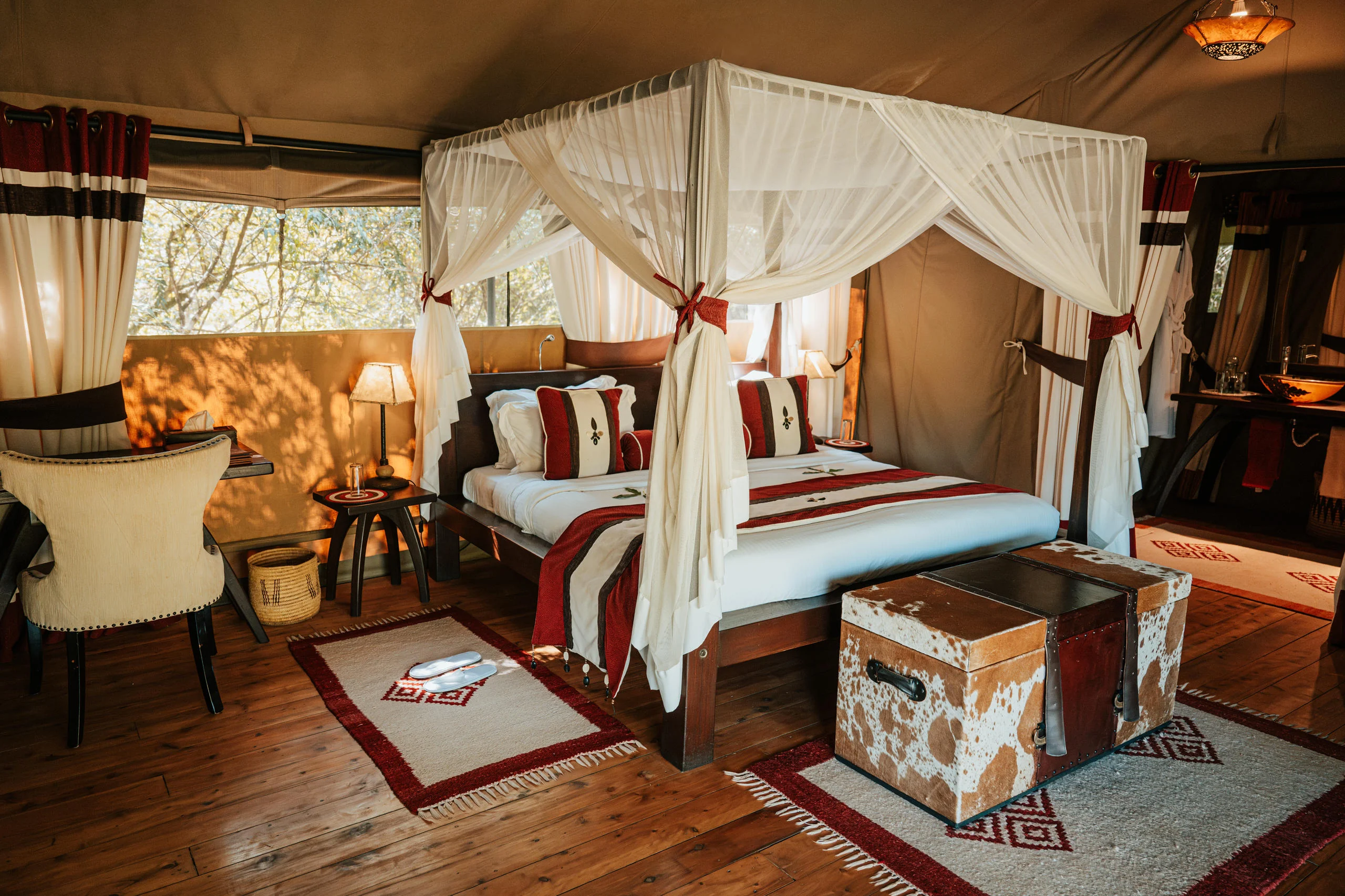 A tent bedroom with twin draped beds and a red rug