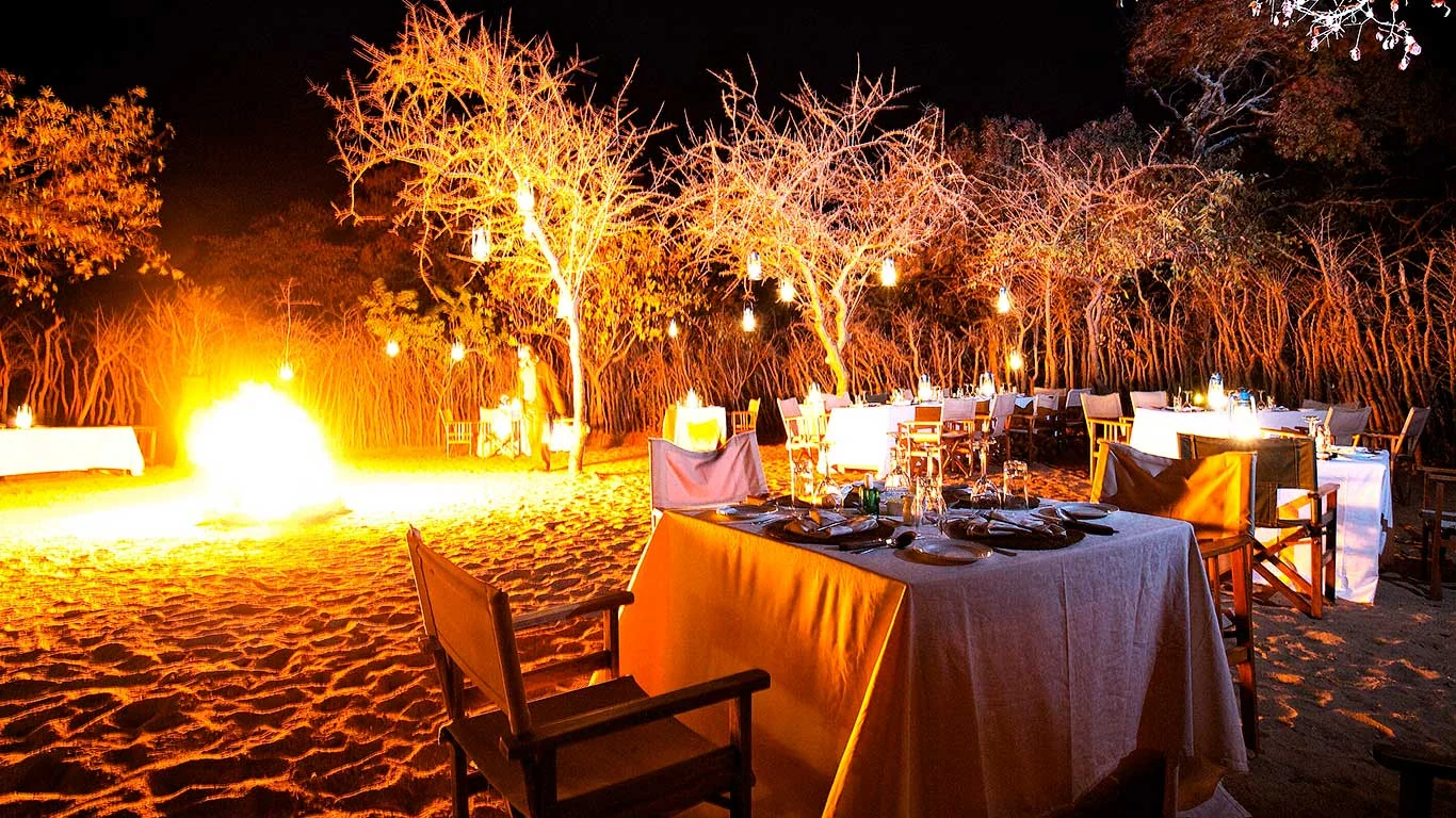 Dinner set out in the bush, lit by a fire and lanterns