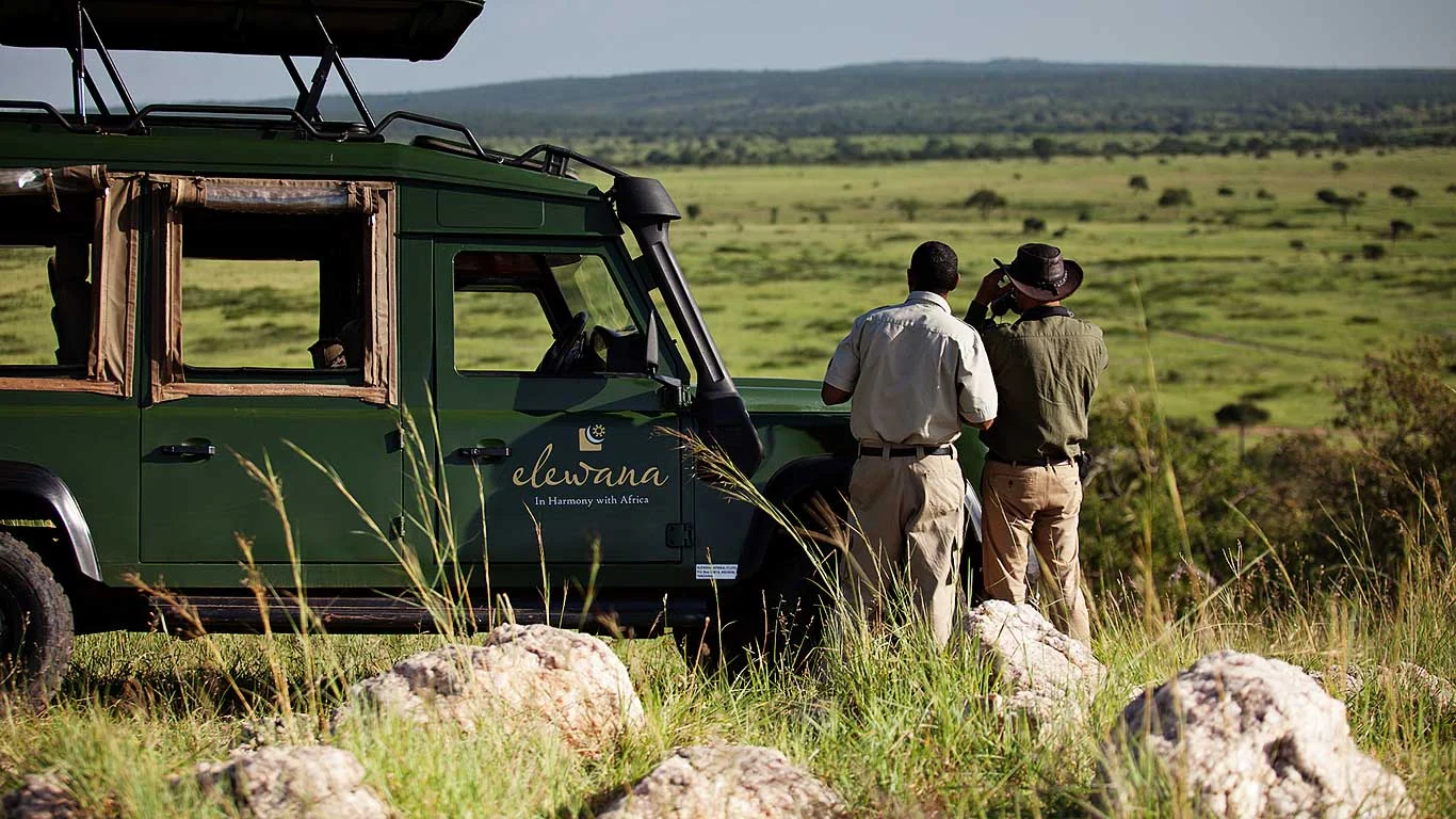 Guides beside a safari vehicle overlooking the plains