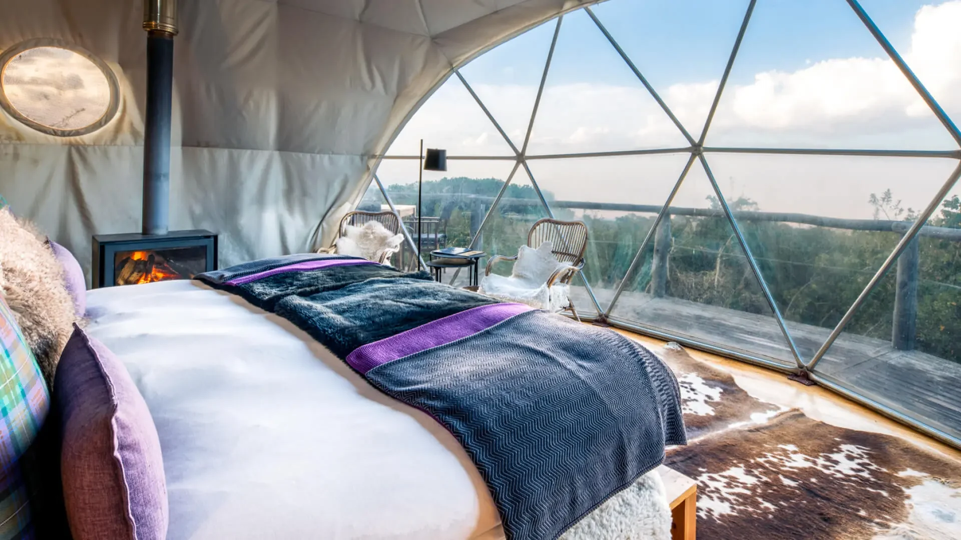 A bed beside the dome's window, with the view beyond
