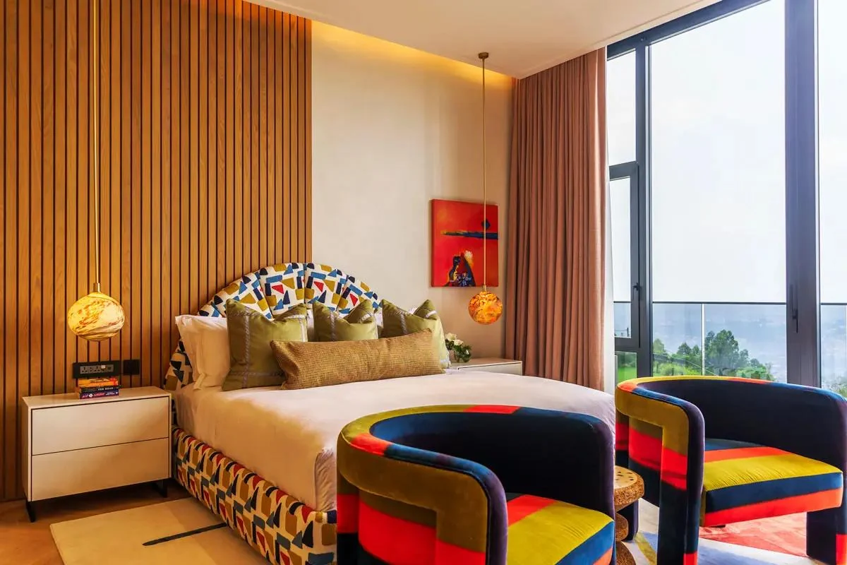 A bedroom with patterned armchairs and windows onto the city
